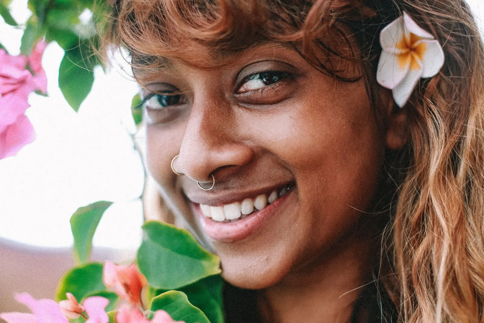 Close-up portrait of a smiling woman with flowers in her hair, exuding natural beauty.